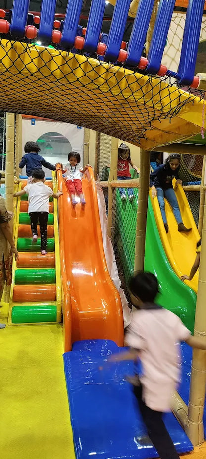 Children play on slides and climbing structures in a colorful indoor playground.
