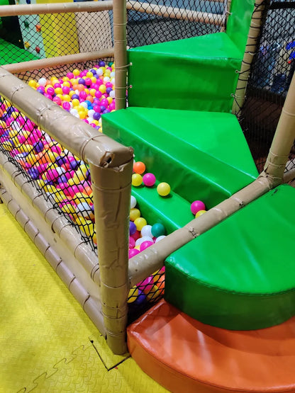 A colorful ball pit in a children's play area with green steps and padded flooring.