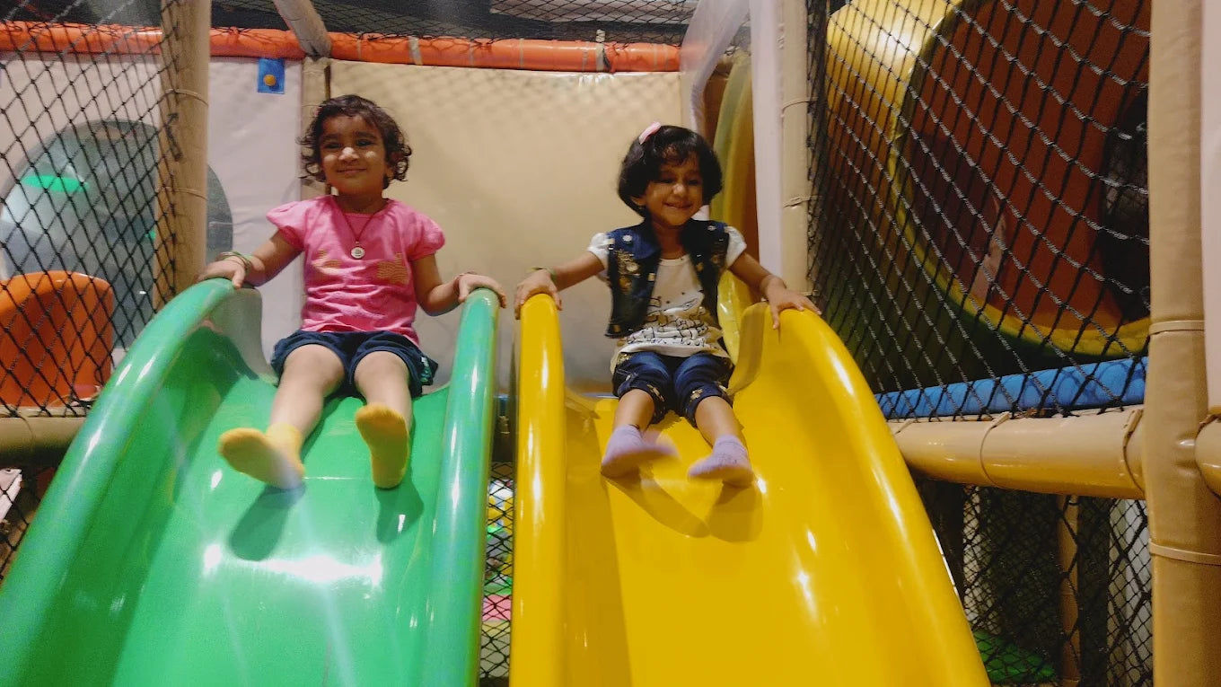 Two young girls slide down colorful playground slides.