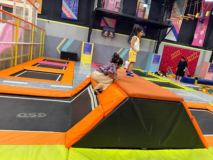 Children playing on trampolines in an indoor playground with colorful walls and banners.
