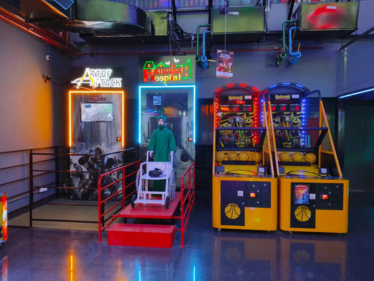 A person in a green costume sits in a wheelchair in front of arcade games.