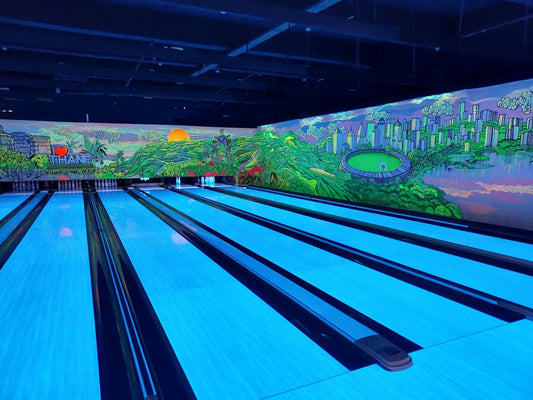 A neon-lit bowling alley with a mural of a city and mountains.