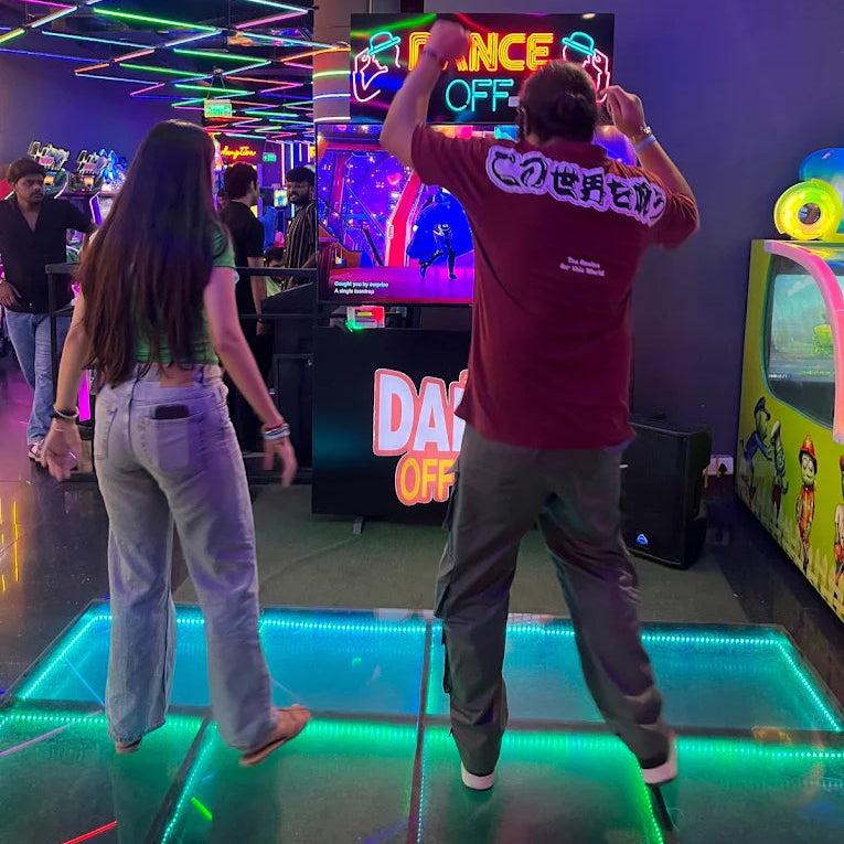 Two people playing an arcade game with colorful lights and decorations in the background.
