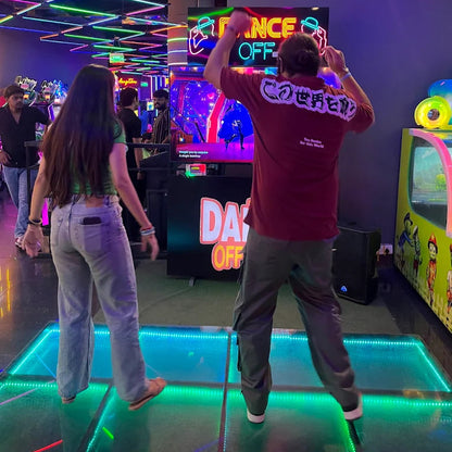 Two people playing an arcade game with colorful lights and decorations in the background.