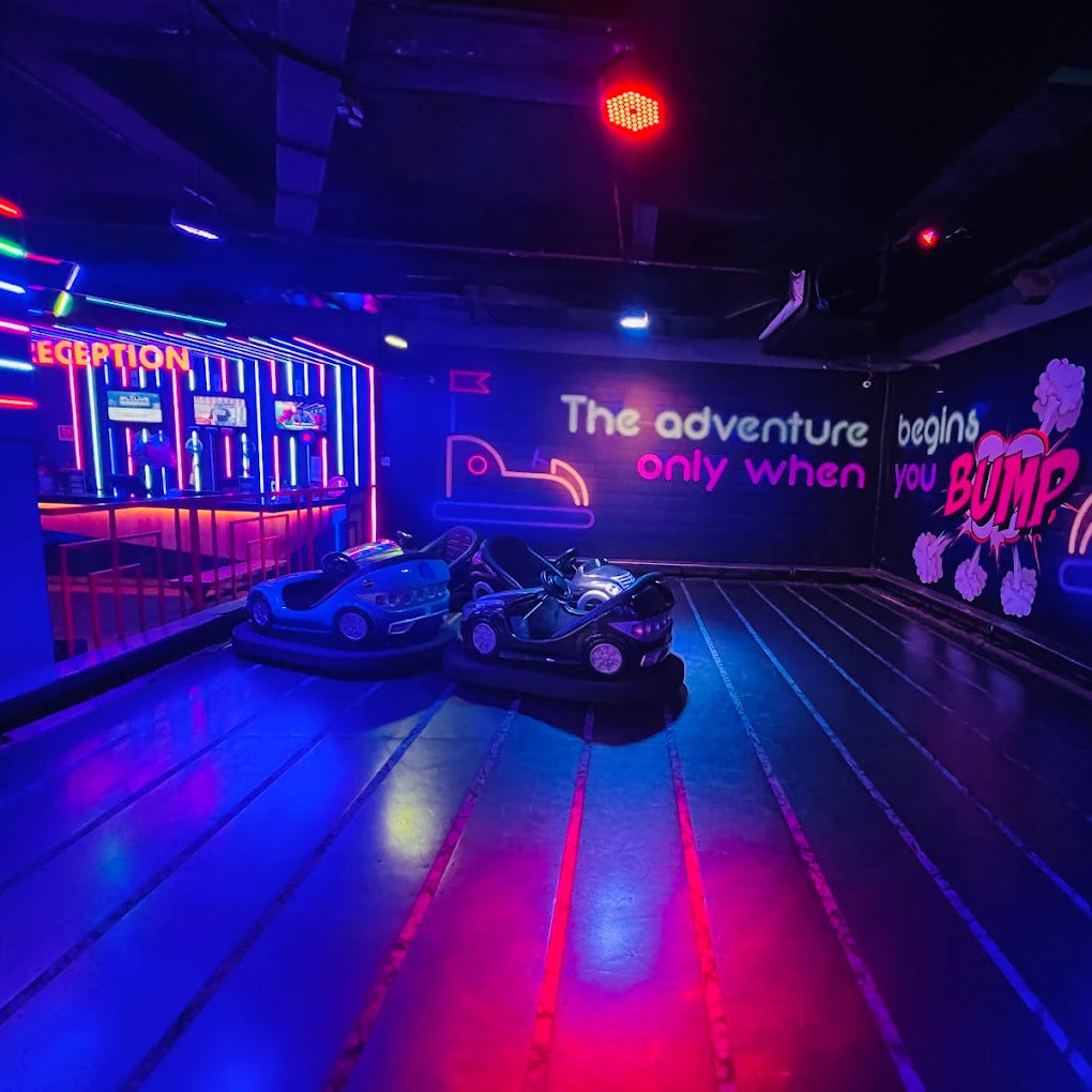 Indoor amusement area with bumper cars and neon lights, featuring a motivational quote on the wall.