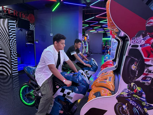 Two young people play a motorcycle racing arcade game in a brightly lit entertainment center.