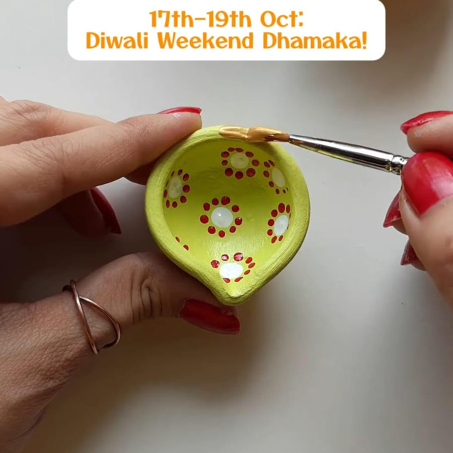 Person painting a decorative diya with red patterns on a white background, promoting Diwali Weekend Dhamaka event.