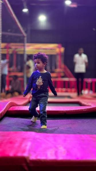 A young child jumps on a trampoline in a dimly lit indoor play area.