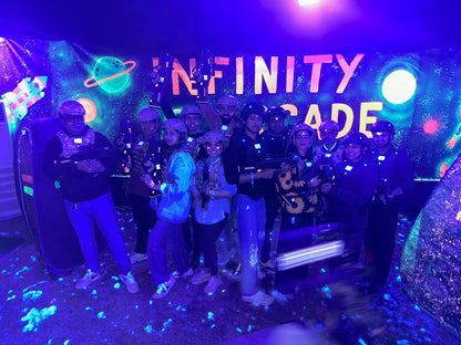 A group of young adults plays laser tag in a neon-lit arcade with a space-themed backdrop.