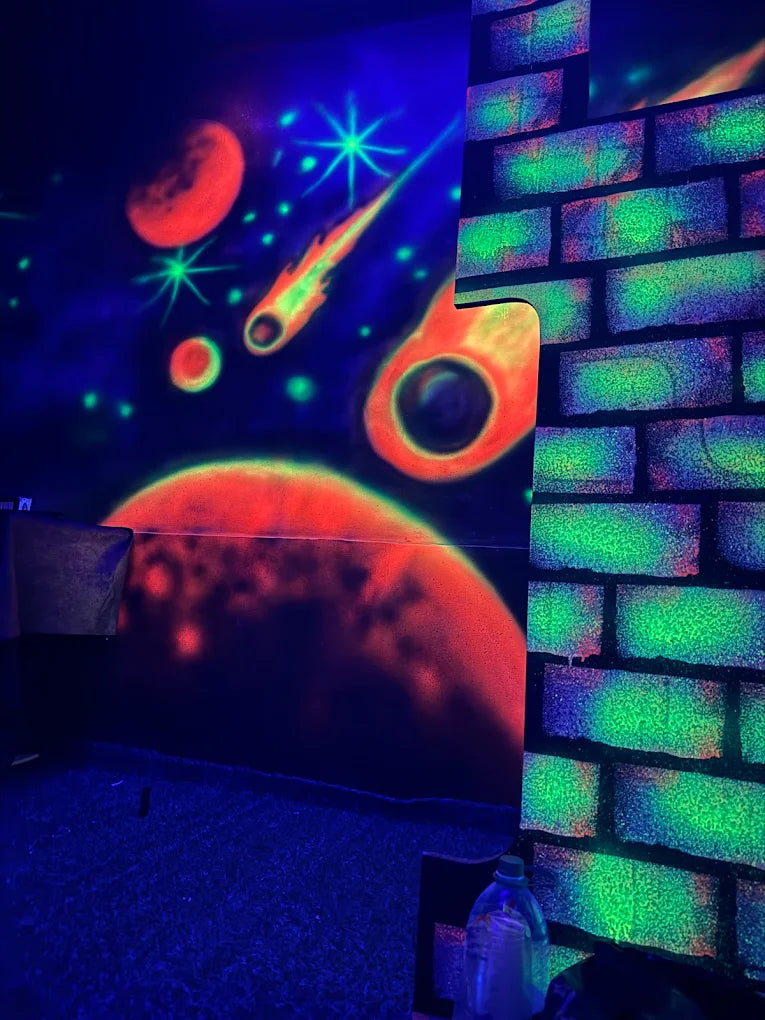 A neon-lit room with space-themed murals and a brick wall.