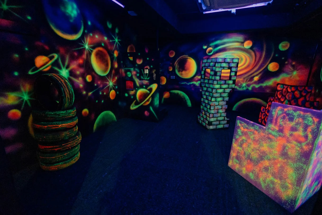 A dark room with neon space-themed murals and obstacles, likely for a laser tag game.