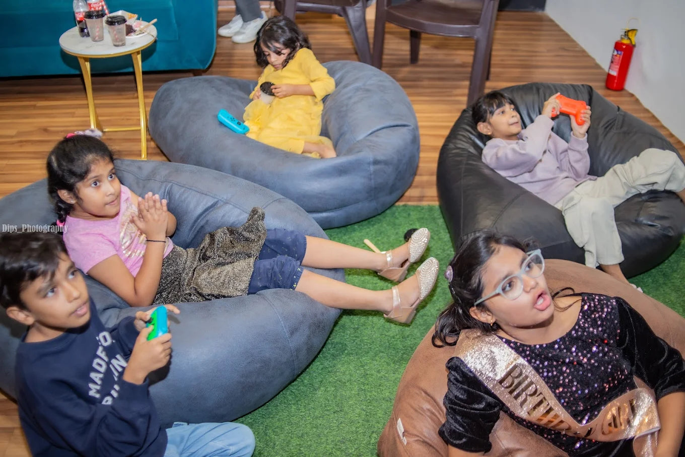 Children play video games on beanbag chairs at a party.