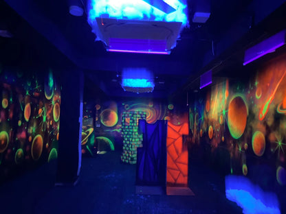 A dark laser tag arena with neon space-themed murals and glowing obstacles.