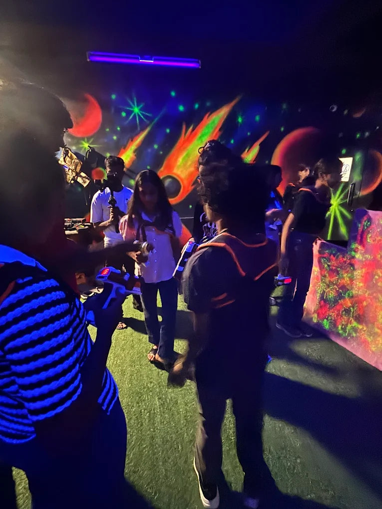 A group of young people in a dimly lit laser tag arena, wearing glowing vests and holding phasers.