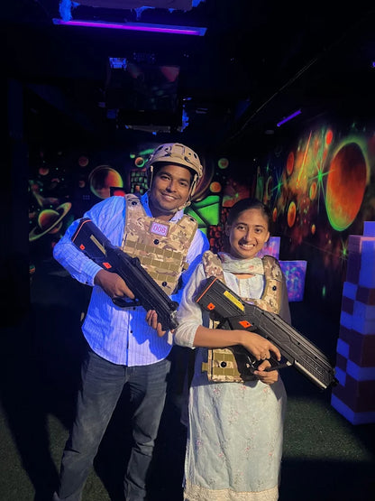 Two young adults in a laser tag arena, wearing vests and holding phasers.
