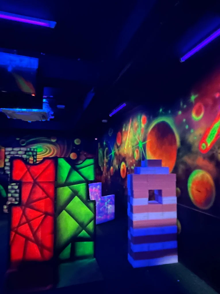 A neon-lit laser tag arena with colorful walls and obstacles.