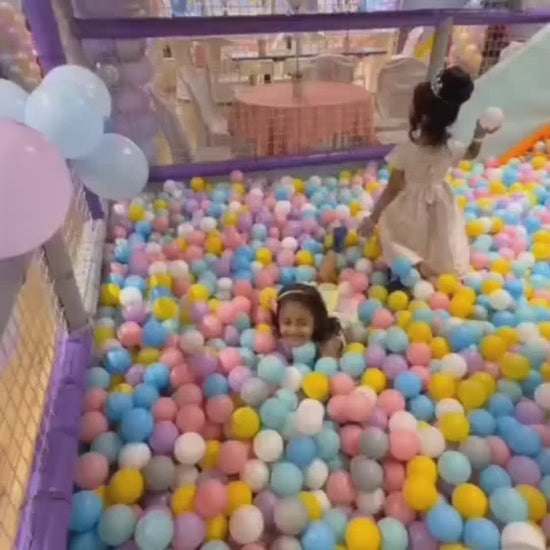 Children play in a vibrant indoor playground filled with colorful balls, slides, and soft play structures. Toddlers and young children enjoy bouncing, sliding, and building, creating a lively and joyful atmosphere.