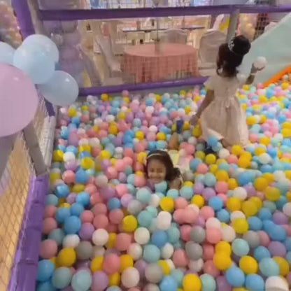 Children play in a vibrant indoor playground filled with colorful balls, slides, and soft play structures. Toddlers and young children enjoy bouncing, sliding, and building, creating a lively and joyful atmosphere.