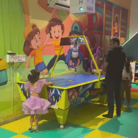Children of various ages enjoy a vibrant indoor play area filled with colorful ball pits, slides, trampolines, and arcade games. The atmosphere is lively and energetic, with kids actively engaged in play. The environment is designed for fun and recreation, featuring bright murals and a variety of play equipment.
