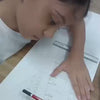 Young artists concentrate on their drawings in a bright, well-lit studio. The atmosphere is focused and creative, with students of various ages diligently working on their art. Tools like rulers, pencils, and sketchbooks are visible, showcasing the artistic process.