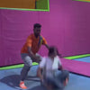 A group of young people enjoys a trampoline park, engaging in activities like jumping, sliding down a ramp, and playing in a ball pit. The vibrant, colorful setting features various attractions, including climbing walls and robotic boxing games. The atmosphere is energetic and fun, with participants of different ages actively participating in the recreational activities.