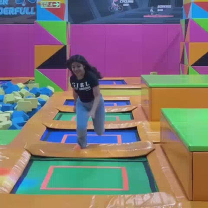 A young person enjoys a trampoline park, navigating obstacles and a foam pit. The vibrant, colorful environment features trampolines, climbing walls, and slides. The atmosphere is energetic and fun, with people of various ages participating.