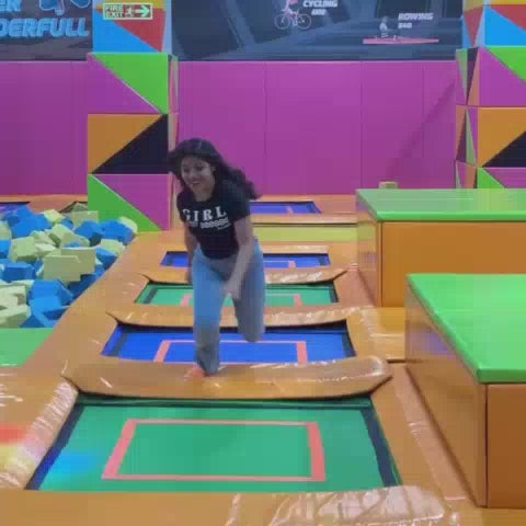A young person enjoys a trampoline park, navigating obstacles and a foam pit. The vibrant, colorful environment features trampolines, climbing walls, and slides. The atmosphere is energetic and fun, with people of various ages participating.