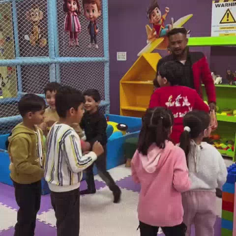 Children of various ages enjoy a vibrant indoor play area filled with colorful balls, slides, and climbing structures. The atmosphere is lively and energetic as kids engage in playful activities like sliding, building, and interacting with each other. Notable features include a ball pit, magnetic building blocks, and a climbing wall.