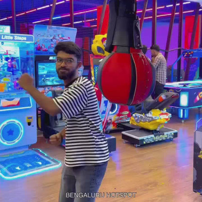 A group of young adults enjoys a vibrant arcade, engaging in various games like VR paragliding, racing simulators, and a claw machine. The atmosphere is energetic, with colorful lights and exciting attractions filling the space.