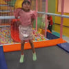 Children of various ages enjoy a vibrant indoor play area filled with colorful balls, trampolines, and climbing structures. The atmosphere is lively and playful, with kids actively engaged in climbing, jumping, and imaginative play. The environment is designed for fun and exploration, featuring bright decorations and interactive elements.