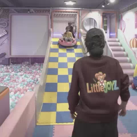 A vibrant indoor play area with a ball pit, slides, and interactive games. Children of various ages enjoy activities like sliding, playing in the ball pit, and a climbing wall. The atmosphere is lively and fun, with colorful decorations and engaging attractions.
