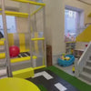 Children engage in playful activities like sliding and climbing in a brightly colored indoor playground. The environment features soft play structures, a ball pit, and a mini kitchen, creating a fun and stimulating atmosphere for young children.