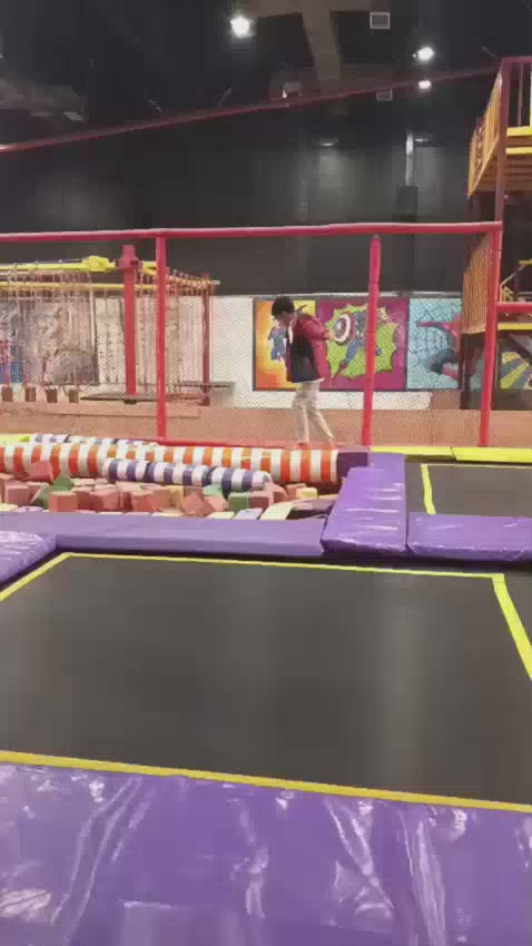 Multiple kids & teens jumping on trampoline and playing game of tag using foam blocks.