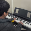 A young boy plays a digital piano in a room with a light-colored wall. The atmosphere is focused and calm as he practices his music.