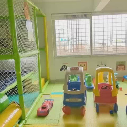 Children of various ages enjoy a vibrant indoor play area filled with colorful balls, slides, and climbing structures. The setting is a lively and safe environment designed for active play and fun. Notable features include a ball pit, a climbing wall, and a soft play structure.
