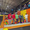 A vibrant indoor trampoline park buzzes with energy as people of various ages leap and play. Colorful foam pits, climbing walls, and basketball hoops are among the attractions. The atmosphere is lively and fun, with a mix of children and adults enjoying the active environment.
