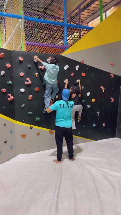 Kids and adults enjoying indoor rock climbing at a family play area with safety harnesses and padded flooring