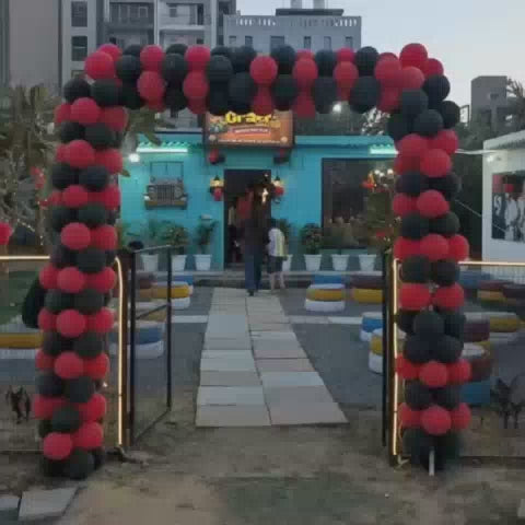 A vibrant outdoor cafe, decorated with balloons and tire seating, hosts various activities. Children and adults engage in remote-controlled car racing on a track and pottery making, creating a lively and fun atmosphere.