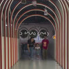 A family enjoys a vibrant indoor play area with interactive games, a ball pit, and slides. Children of various ages engage in digital hopscotch, coloring, and climbing walls, creating a lively and fun atmosphere. The setting features bright projections, colorful decor, and comfortable seating for parents.