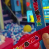 Children enjoy arcade games and a ball pit at a vibrant indoor play center. The atmosphere is lively with colorful lights and engaging attractions like a dinosaur shooting game and a police car. Younger children are seen playing in a ball pit and on a mini car, while older kids are engrossed in arcade games.