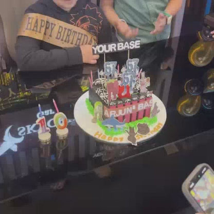 A birthday celebration at a gaming cafe features a cake with dinosaur decorations and "Happy Birthday" toppers. Children and teens are seen playing video games on multiple screens, some wearing headphones, creating a lively and fun atmosphere. The cafe is decorated with balloons and has a "Skycrest Gaming Cafe" sign.