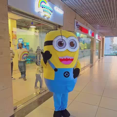 A lively indoor play cafe buzzes with children of various ages enjoying a birthday party. Attractions include a ball pit, slides, arcade games, and a Minion mascot, creating a festive and energetic atmosphere.