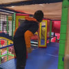 A young boy gleefully navigates a vibrant indoor playground filled with colorful slides, a ball pit, and interactive games. He swings, climbs, and slides through various attractions, enjoying the energetic atmosphere. The playground appears designed for children, with soft surfaces and engaging activities.