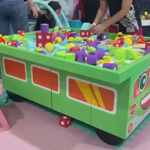 Children of various ages are joyfully engaged in a vibrant indoor play area filled with colorful toys, soft play structures, and ball pits. The atmosphere is lively and fun, with kids actively participating in activities like building, sliding, and climbing. The setting is a well-equipped play zone designed for entertainment and engagement, featuring a ball pit, a trampoline, and interactive play stations.