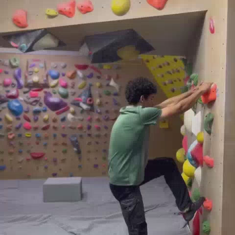 Young adults enjoy a challenging bouldering session in a vibrant indoor climbing gym, with colorful holds adorning the walls and a supportive atmosphere. The scene captures moments of intense focus, athletic movement, and camaraderie among the climbers.