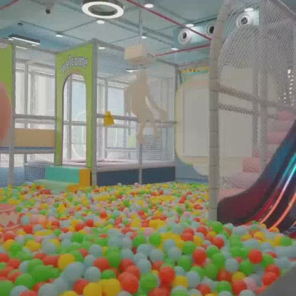 A vibrant indoor play area filled with colorful balls, slides, and play structures. Children of various ages enjoy activities like sliding, jumping on trampolines, and playing pretend in themed areas like a fire station and police station. The atmosphere is lively and fun, with families interacting and children engaged in playful exploration.