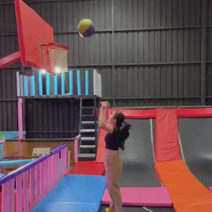 A young woman enjoys various activities at a trampoline park, including basketball, navigating a rope maze, and riding bumper cars. The vibrant indoor space features trampolines, foam pits, climbing walls, and colorful decorations, creating a fun and energetic atmosphere for all ages.