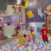Children of various ages enjoy a vibrant indoor playground filled with slides, ball pits, and climbing structures. The atmosphere is lively and playful, with kids engaging in activities like sliding, bouncing, and interacting with a costumed character. The colorful environment, featuring space-themed decorations, adds to the fun and excitement.