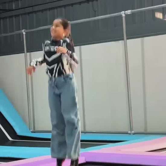 A young girl enjoys a variety of interactive exhibits at an indoor amusement park. She bounces on trampolines, swings on a rope, plays with a ball machine, and tries a "stringless harp." The atmosphere is lively and fun, with colorful attractions and other children present.