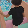 A young child enjoys a vibrant indoor playground filled with colorful balls, slides, and interactive musical instruments. The atmosphere is playful and energetic, with various age groups engaging in different activities. Notable features include a ball pit, a large slide, a musical piano mat, and a water play area.